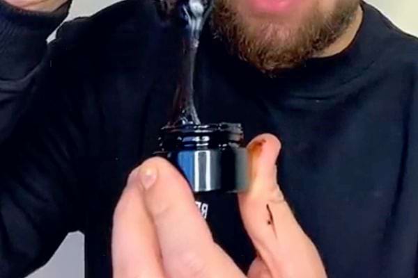 Homme extrayant une résine noire visqueuse d'un pot de Shilajit.