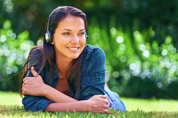Une femme souriante allongée sur l'herbe, écoutant de la musique avec des écouteurs.