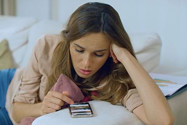 Une femme allongée regarde son téléphone avec une expression préoccupée.