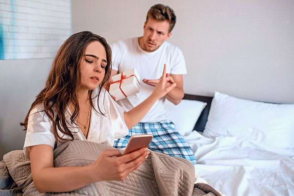 Un homme lève un doigt en signe d'avertissement vers une femme concentrée sur son téléphone.