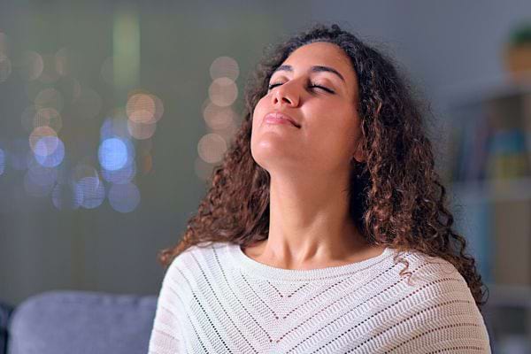 Une femme les yeux fermés, la tête inclinée en arrière, respire profondément.