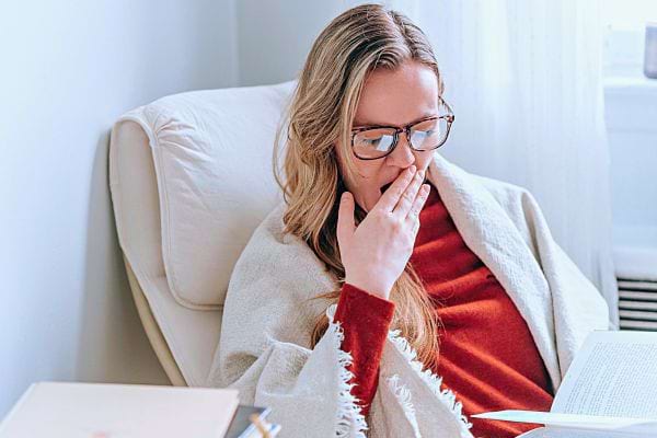 Une femme paraissant fatiguée tout en lisant un livre, symptôme de fatigue inexpliquée.
