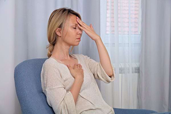 Une femme semble avoir un mal de tête, main sur le front, yeux fermés.