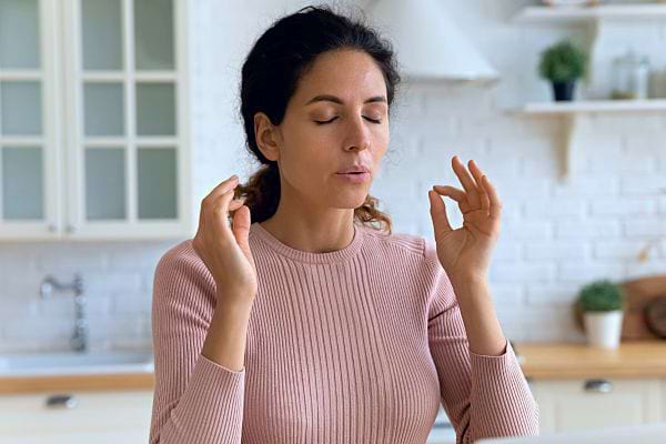Une femme souffle pour se calmer, les yeux fermés, les doigts sur les tempes.