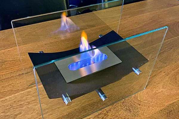 Cheminée bioéthanol de table compacte avec panneaux en verre et supports en acier.