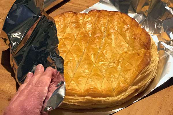 Une galette des Rois enveloppée de papier aluminium, partiellement dévoilée, indiquant une méthode de conservation.