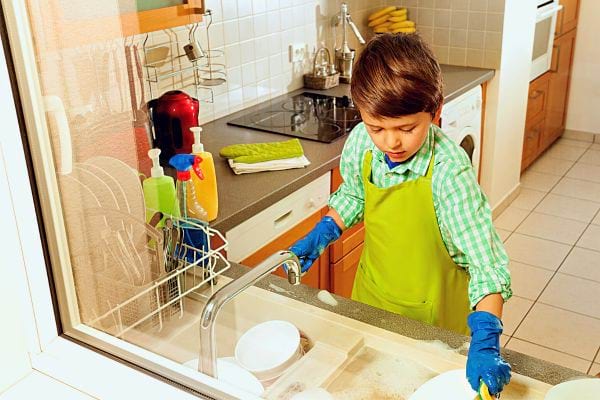 Un garçon en tablier vert fait la vaisselle, apprenant les responsabilités domestiques.