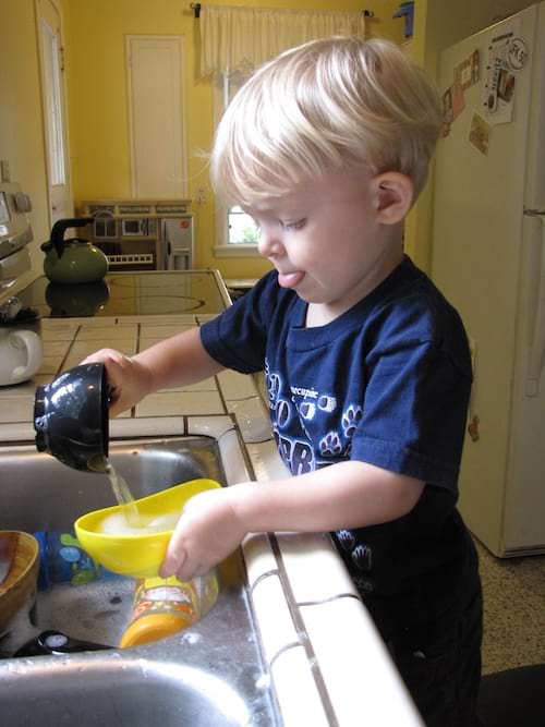 Un petit garçon verse du savon à vaisselle, s'amusant tout en aidant à la maison.