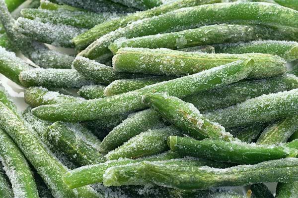 Haricots verts surgelés éparpillés avec des cristaux de glace visibles.