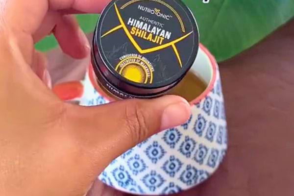 Main tenant un pot de Shilajit avec couvercle jaune et étiquette NutroTonic.