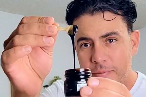 Homme tenant une spatule avec de la résine de Shilajit étirée au-dessus d'un pot.