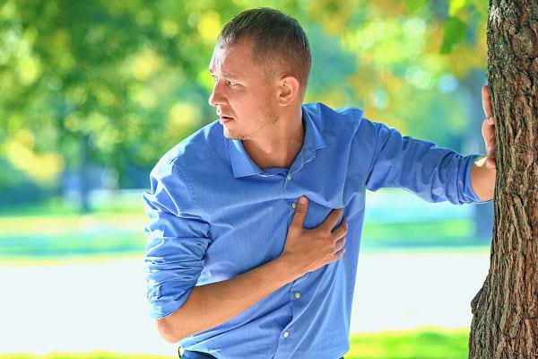 Un homme en chemise bleue, appuyé contre un arbre, semble avoir des palpitations.