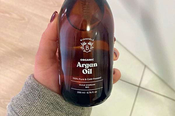 Main tenant une bouteille d'huile d'argan biologique.