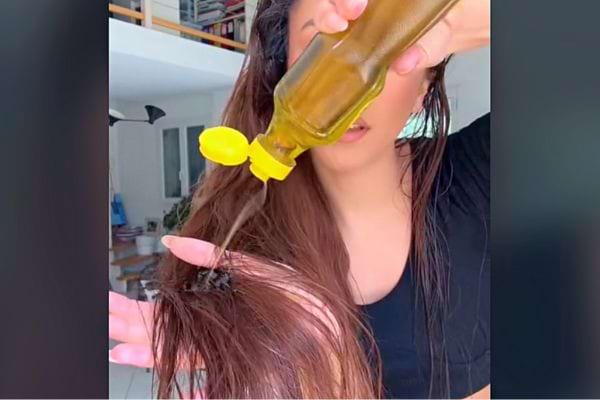 Huile étant appliquée sur des cheveux longs et bruns à l'aide d'une bouteille avec un bec verseur.
