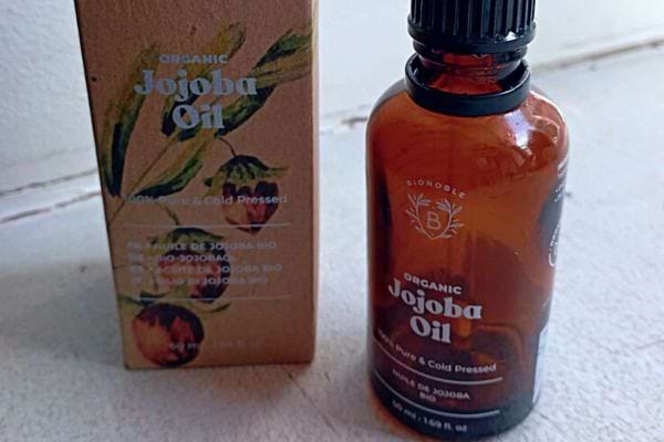 Huile de jojoba biologique à côté de son emballage en carton.