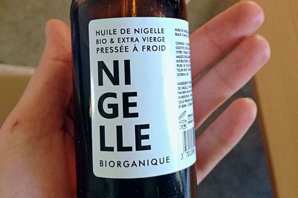 Bouteille d'huile de nigelle biologique et extra vierge tenue en main.