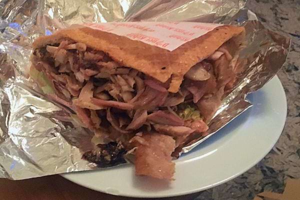 Texte alternatif 1 : Kebab emballé dans du papier aluminium avec de la viande émincée visible, sur une assiette blanche. Texte alternatif 2 : Sandwich kebab