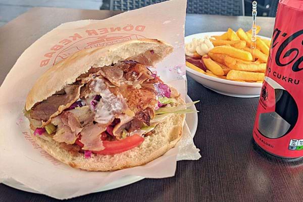 Sandwich kebab dans une assiette avec des frites et une boisson.