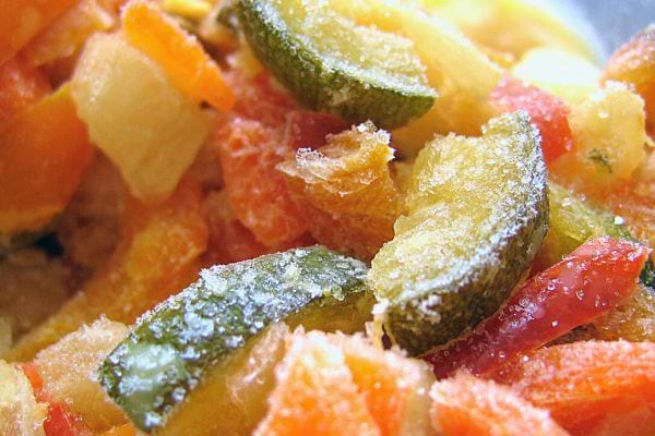 Gros plan de légumes surgelés mélangés, montrant des morceaux de courgettes et de carottes.