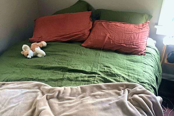 Un lit mal fait avec des draps verts et des oreillers rouges, montrant un lit qui pourrait nécessiter un lavage.