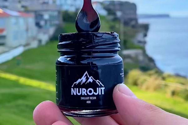 Résine de Shilajit noire coulant d'une cuillère au-dessus d'un pot "NUROJIT".