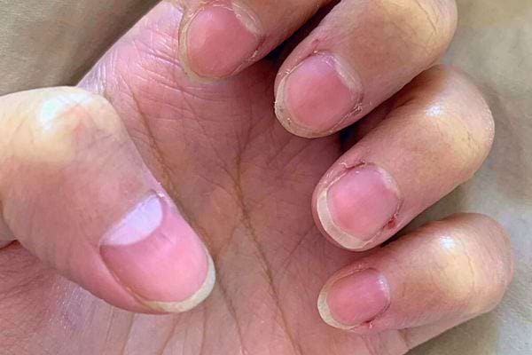 Ongles courts avec une couleur rose naturelle sur une main à la peau légèrement foncée.