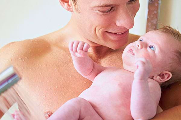 Un père tient un bébé dans ses bras, les deux regardent avec affection.