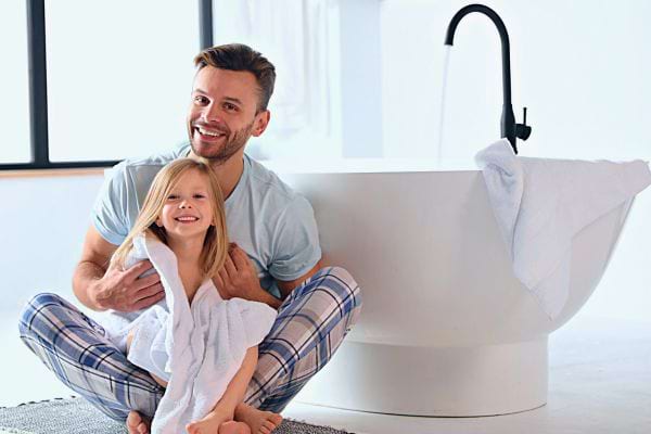 Un père sourit en tenant sa fille dans une serviette après le bain.