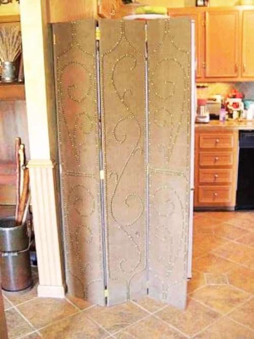 Frigo dissimulé derrière un paravent ornemental, offrant une solution de dissimulation flexible et décorative.