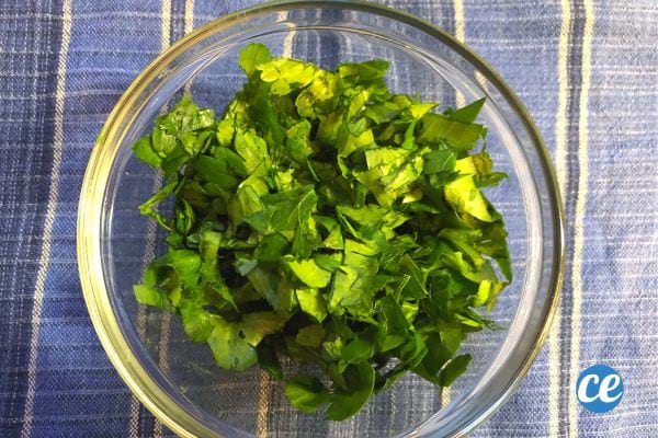 Persil frais haché dans un bol en verre sur une nappe à carreaux bleus.