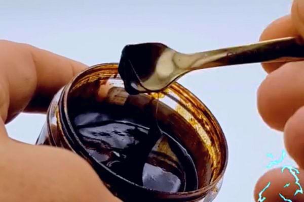 Petite cuillère retirant délicatement de la résine noire d'un pot de Shilajit.