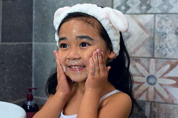 Jeune fille asiatique s'amusant avec de la mousse sur son visage.