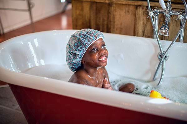 Petite fille noire souriante portant un bonnet de bain dans une baignoire rouge.