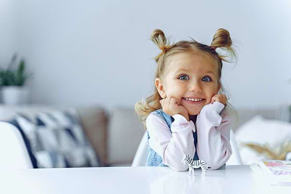 Une petite fille souriante avec des couettes, symbolisant la joie pure et l'importance d'inculquer l'amour de soi.