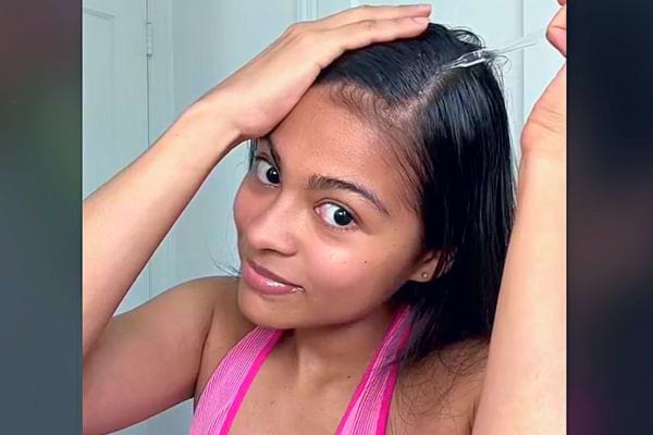 Jeune femme souriante appliquant de l'huile sur sa raie avec une pipette.