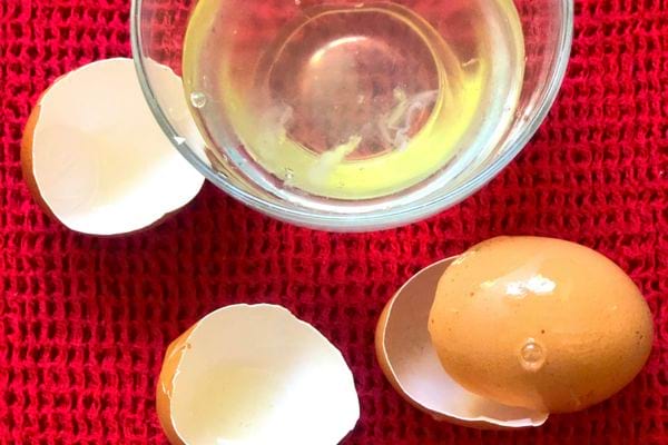 Unordentliche Küche mit zerbrochenen Eierschalen neben einer Glasschüssel auf einem roten Geschirrtuch.