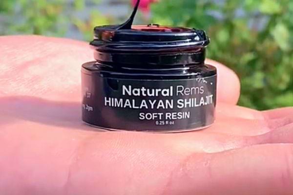 Main tenant un petit pot de Shilajit "Natural Rems" sur fond naturel.