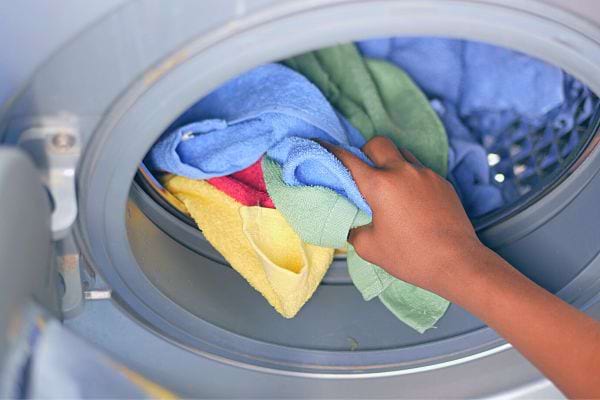 Main mettant des serviettes de couleur vive dans une machine à laver.