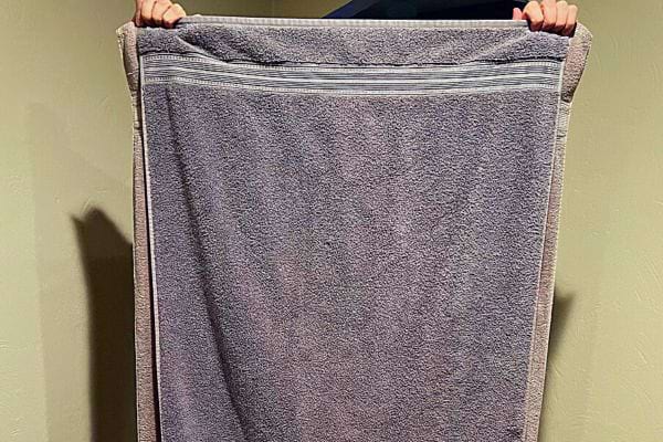 Personne tenant une grande serviette de bain grise dépliée.