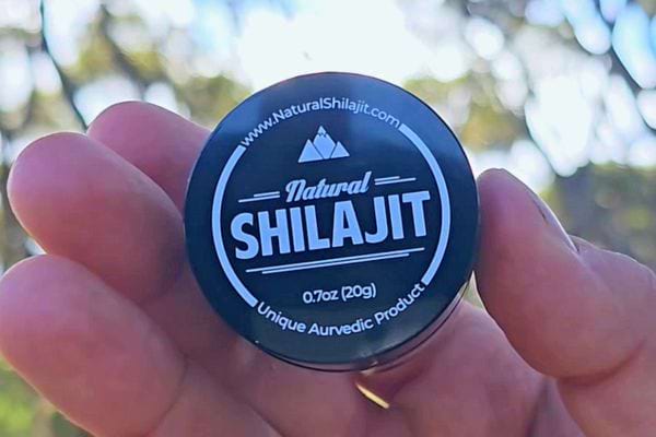 Main tenant un petit pot de Shilajit étiqueté "Natural Shilajit".