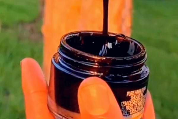 Résine de Shilajit noire luisante étirée depuis un pot ouvert.