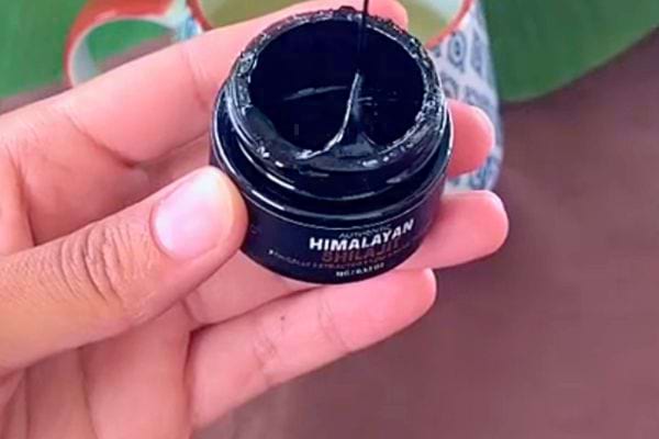 Main tenant un pot ouvert de Shilajit Himalayen avec résine noire brillante.