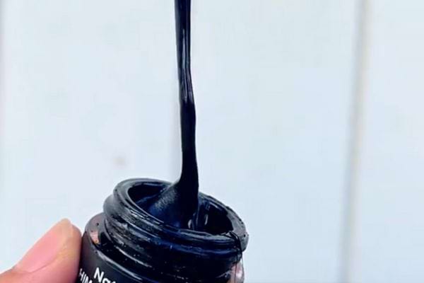 Résine de Shilajit s'étirant verticalement depuis un pot tenu dans une main.