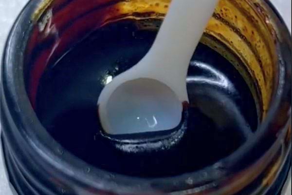 Cuillère blanche prélevant de la résine dans un pot de Shilajit avec couvercle doré.