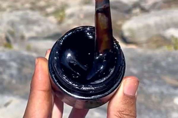 Résine noire de Shilajit coulant dans un pot tenu en main en plein soleil.