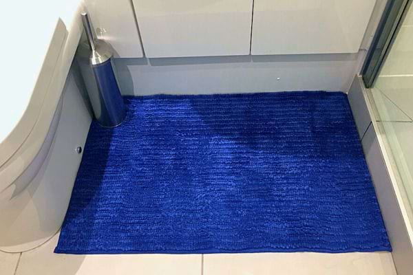 Tapis de bain bleu électrique sur le sol d'une salle de bain moderne.