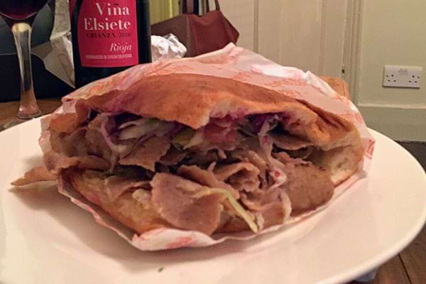 Sandwich kebab ouvert avec une bouteille de vin en arrière-plan.