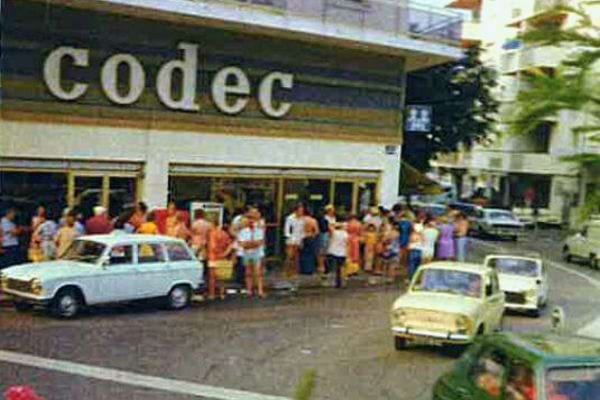 Foule devant un magasin Codec avec une enseigne en lettres capitales sur un bâtiment des années 70.
