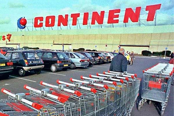 Parking du supermarché Continent avec des chariots et l'enseigne en grandes lettres rouges sur le bâtiment.