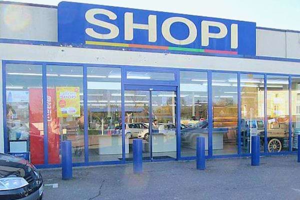 Façade d'un magasin Shopi avec l'enseigne bleue et des fenêtres reflétant le parking.